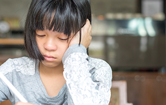 Stock photo of a young, upset girl sitting down and writing.