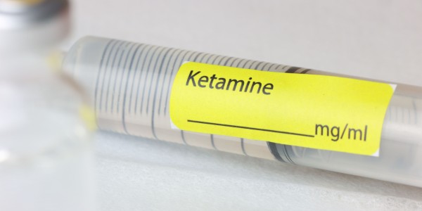 A syringe labeled "Ketamine" beside a vial containing the medication.