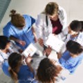 Group of health care professionals standing in a circle and conferring over paperwork.