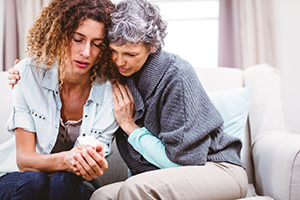 Mother comforting tensed daughter sitting on sofa